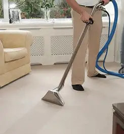 Professional carpet cleaner using a hot-water extraction wand and hose machine in a living room in Long Beach, CA.