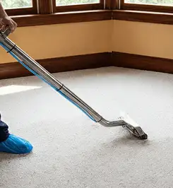 Steam carpet cleaning technician using a hot-water extraction wand on a residential carpet, wearing blue protective shoe covers Long Beach, CA.