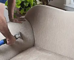 Professional upholstery cleaner deep-cleaning a fabric sofa with a handheld extraction tool and hose in Long Beach, CA.